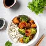 Vegan tofu and broccoli bowl served with rice and chopsticks.