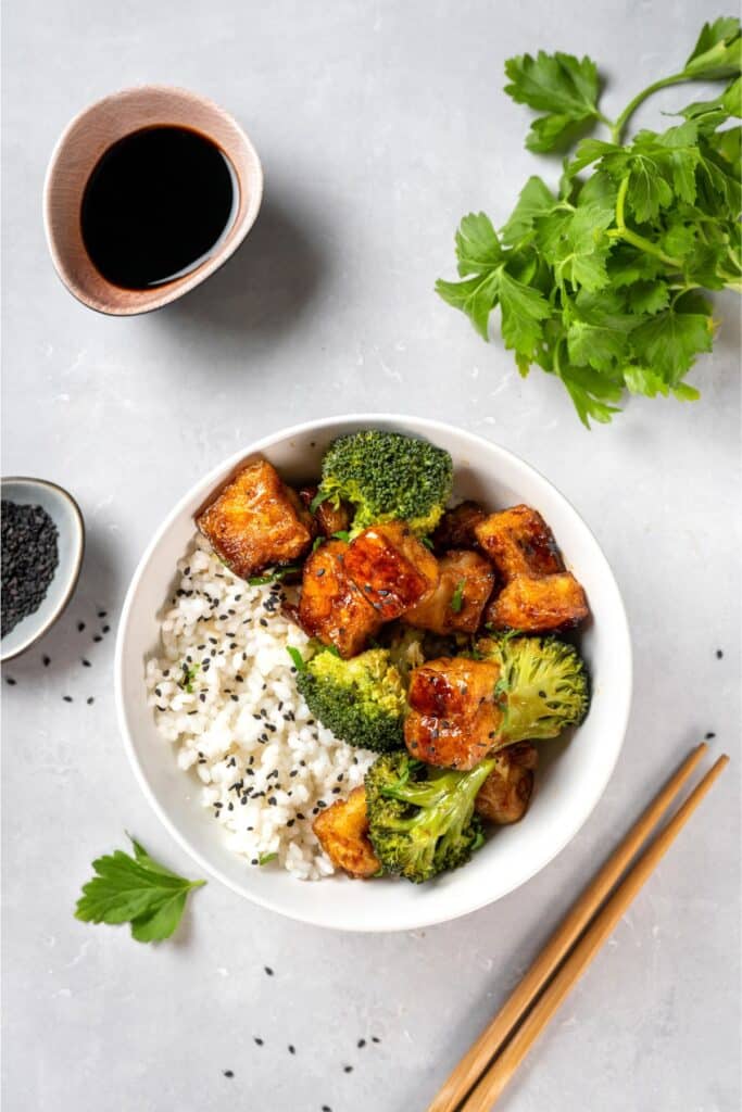 Vegan tofu and broccoli bowl served with rice and chopsticks.
