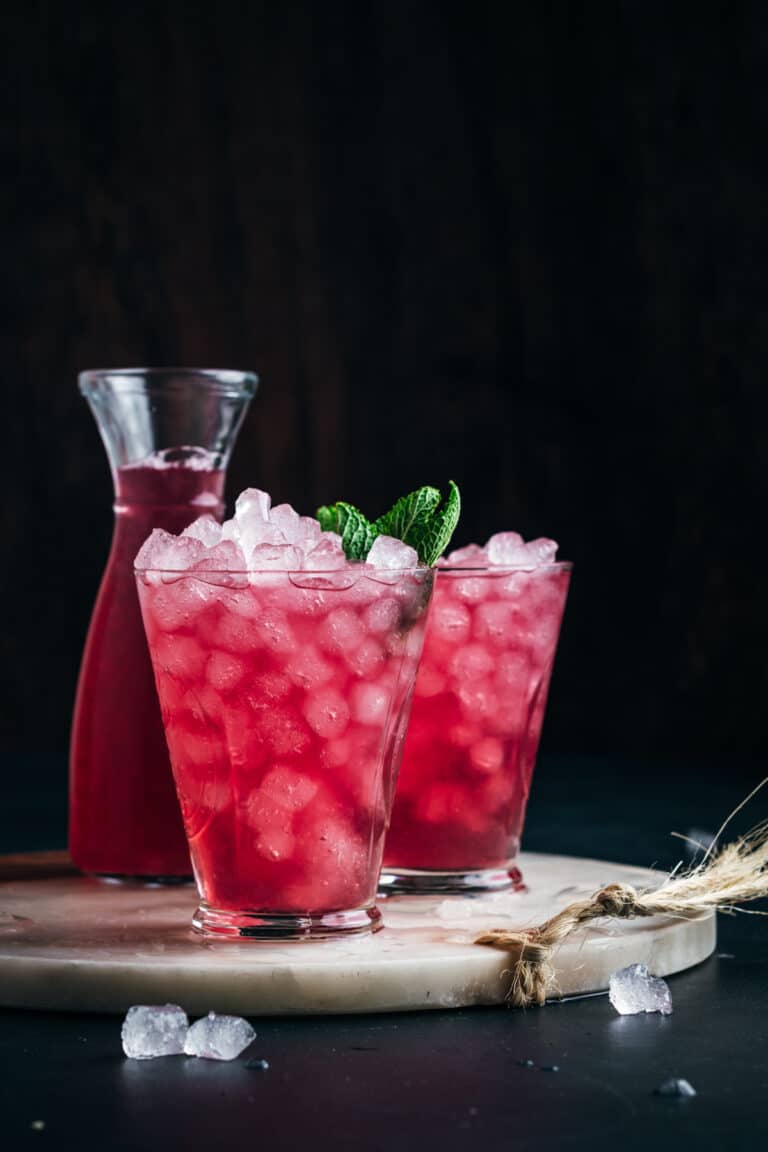 Two glasses of pink iced tea with mint leaves on a wooden board.