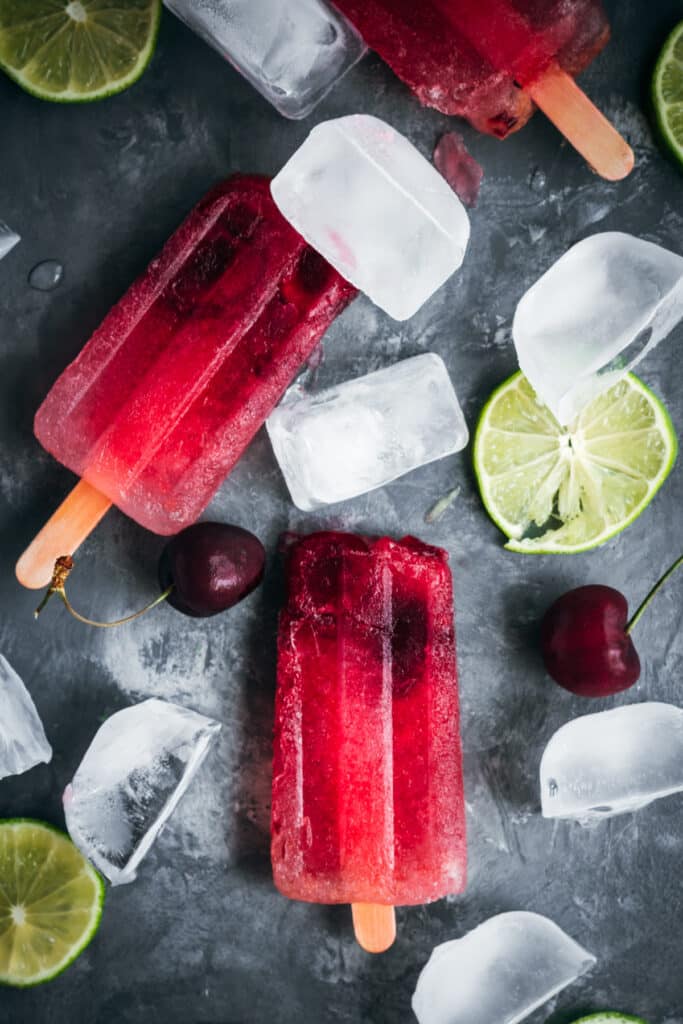 Cherry popsicles with ice cubes and lime slices.