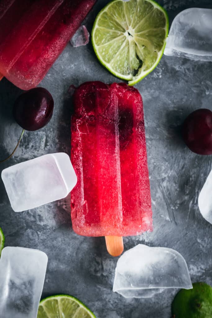 Cherry popsicles with ice cubes and lime slices.