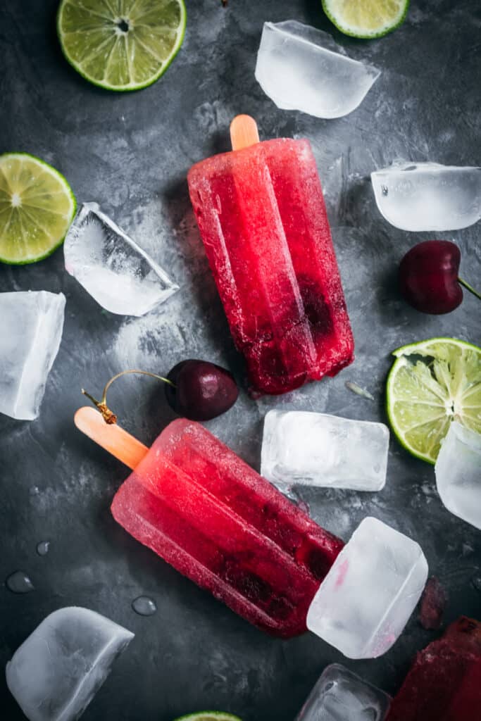 Cherry popsicles on ice with lime slices and ice cubes.