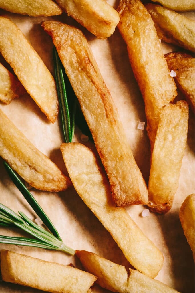French fries with rosemary sprigs on a baking sheet.