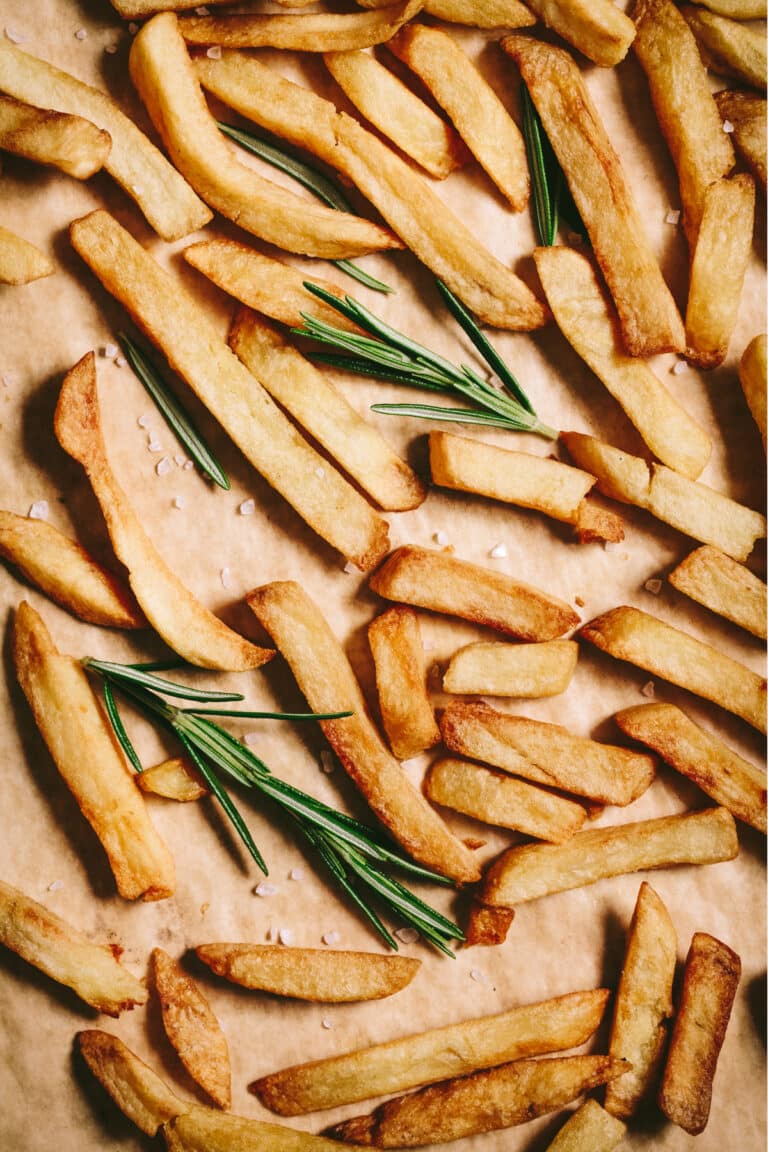 French fries on a baking sheet with rosemary sprigs.