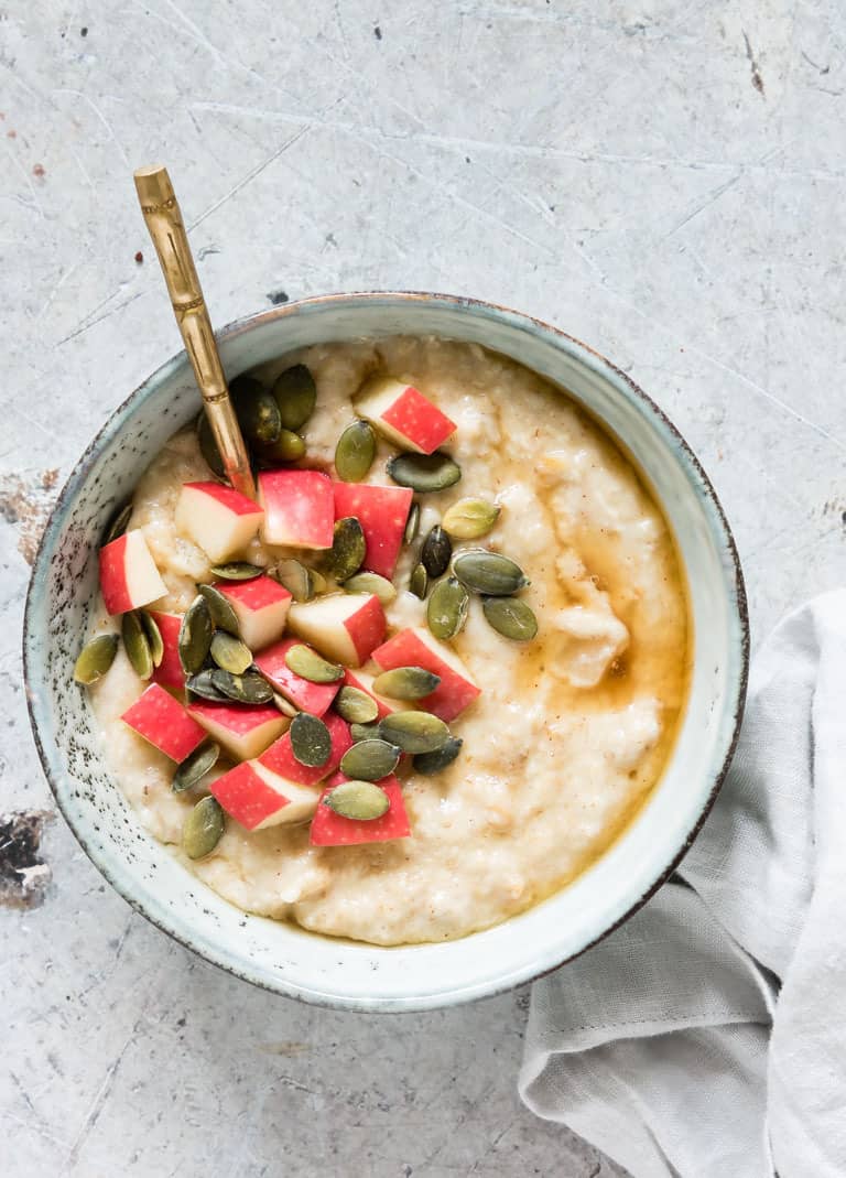 A bowl of oatmeal with apples and pumpkin seeds.