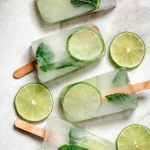 Four popsicles with lime and mint on them.