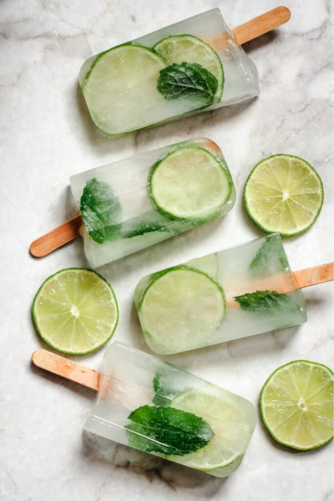 Four popsicles with lime and mint on them.