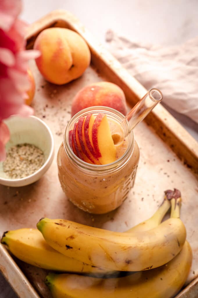 A tray with peaches, bananas and a jar of peach smoothie.