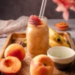 Banana peach smoothie on a wooden tray with peaches.