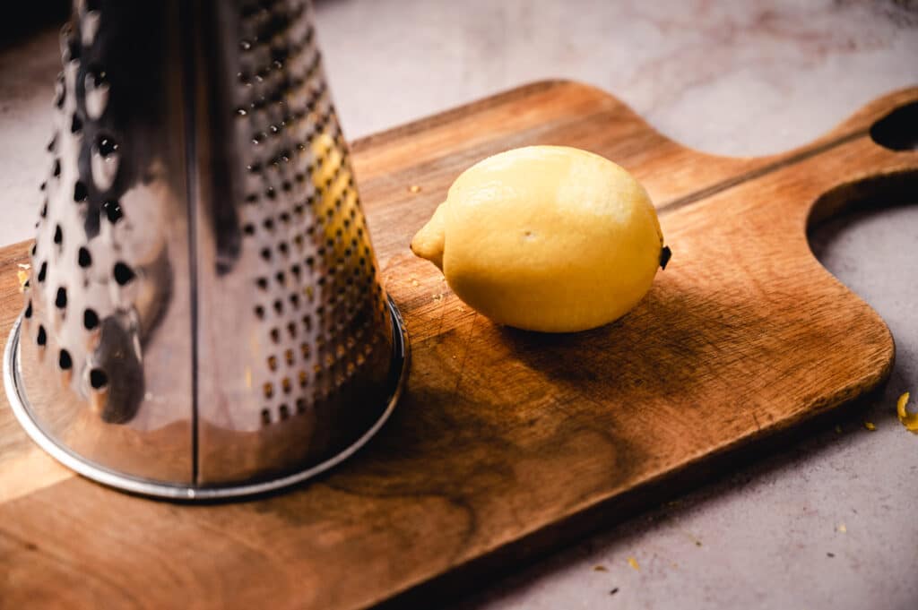 A lemon and a grater on a cutting board.