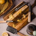 A wooden cutting board with lemons and other kitchen tools.