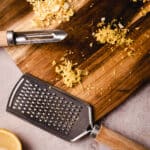 A wooden grater and lemon slices on a wooden cutting board.