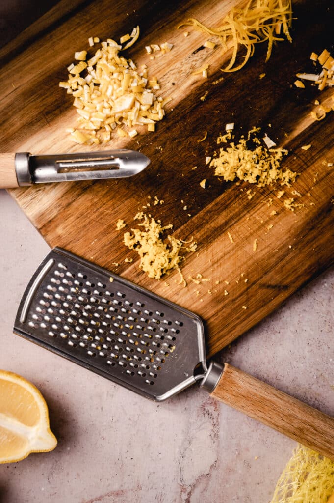 A wooden grater and lemon slices on a wooden cutting board.