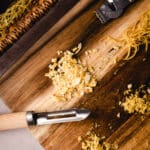 Wood handled vegetable peeler on a cutting board with lemon zest.