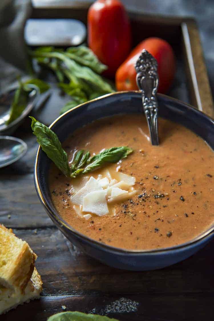 A bowl of tomato soup with bread and basil.