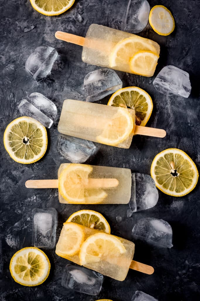 Lemon popsicles with lemon slices and ice cubes surrounding them.