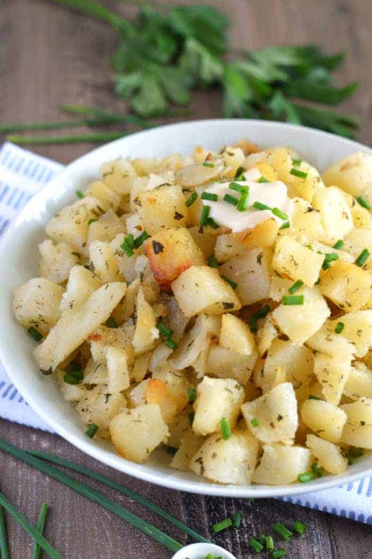 Potatoes in a white bowl with chives and parsley.