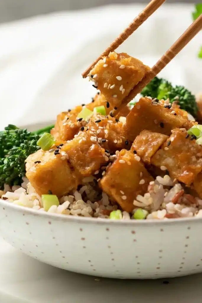Vegan tofu and broccoli dish served in a white bowl with chopsticks.