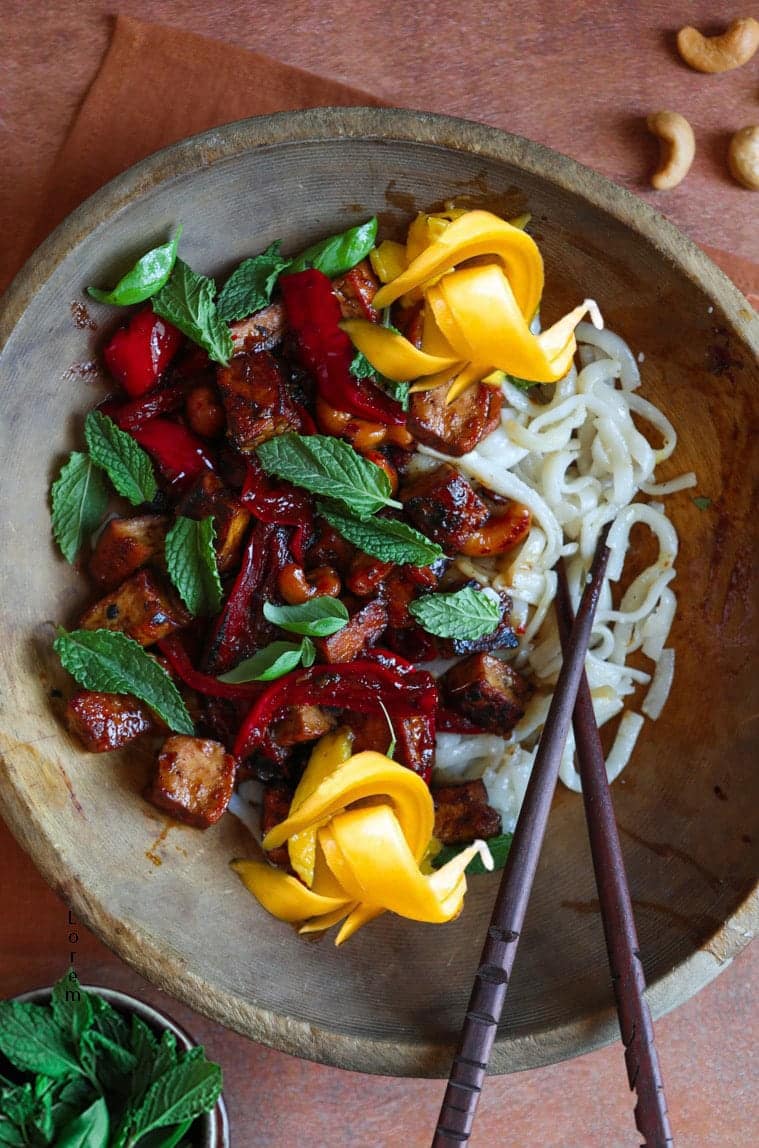 A wooden bowl with noodles and peppers in it.