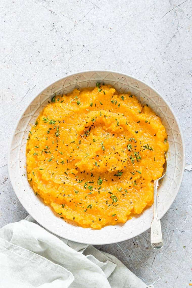 A bowl of sweet potato mashed potatoes with herbs.