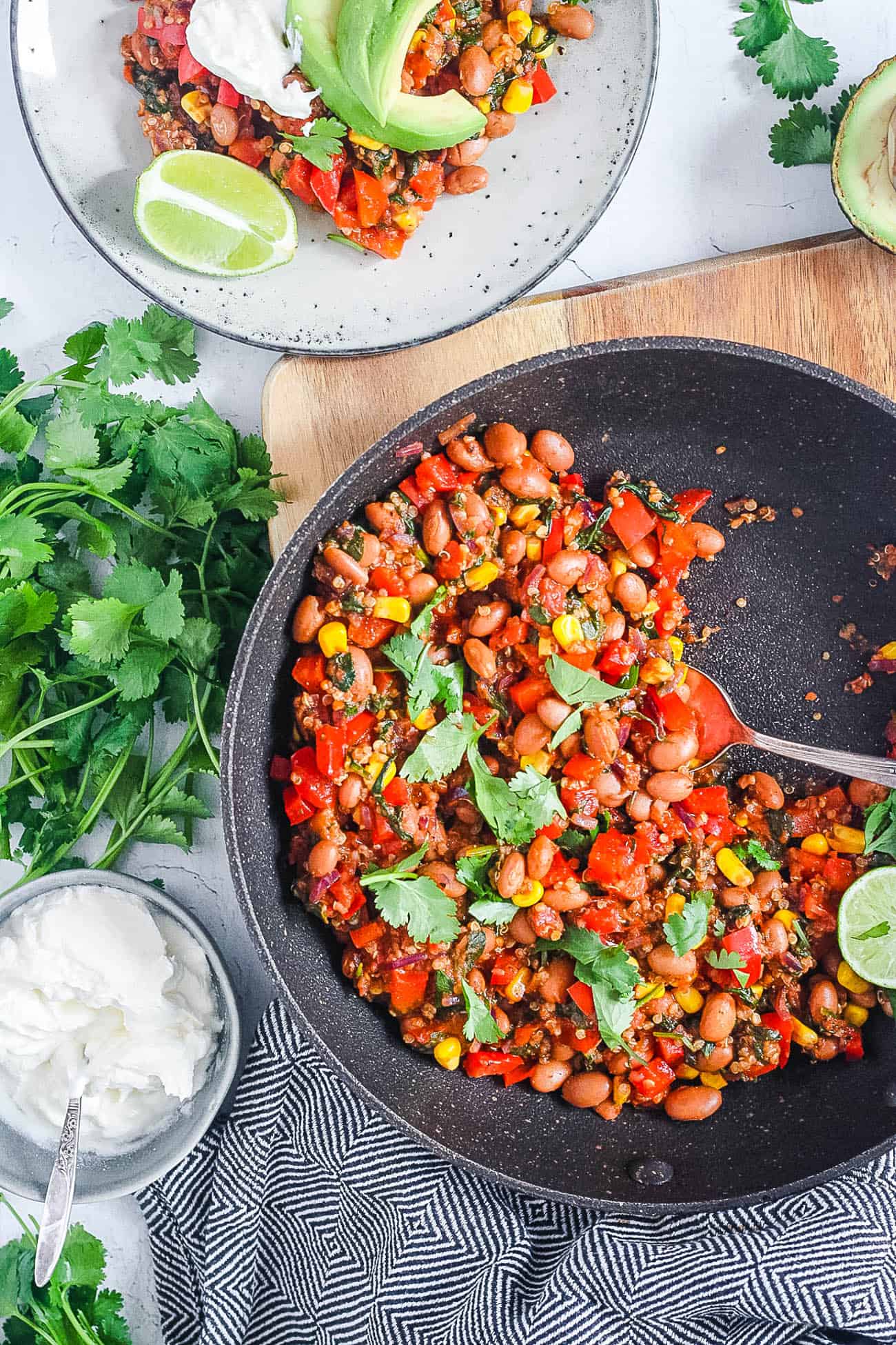 A skillet full of beans and vegetables on a wooden board.