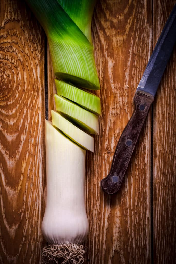 Leek with a knife on a wooden table.