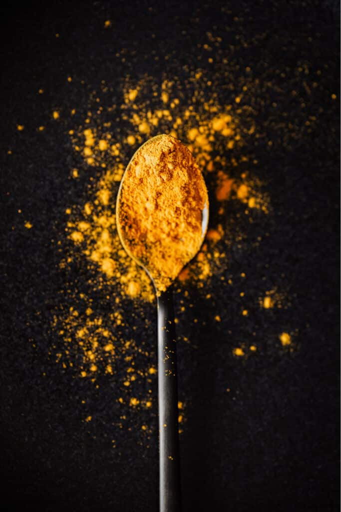 Tumeric powder on a spoon on a black background.