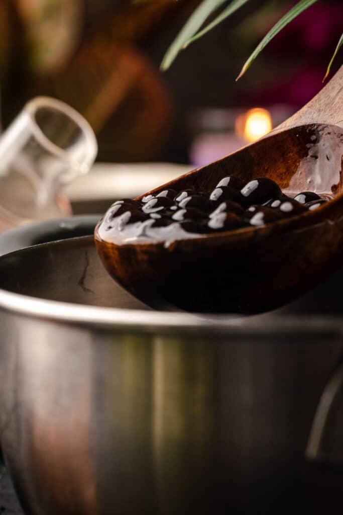 A wooden spoon is being used to stir a bowl of black beans.