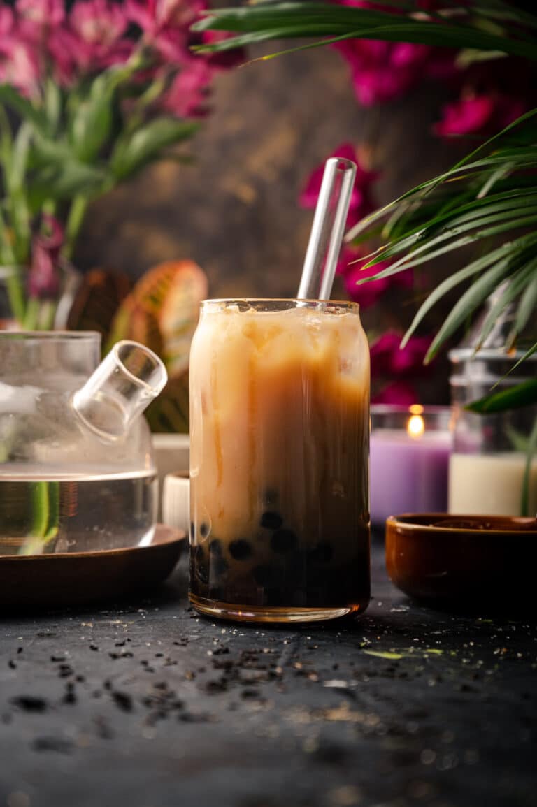 A cup of bubble tea on a table next to a pot of tea.
