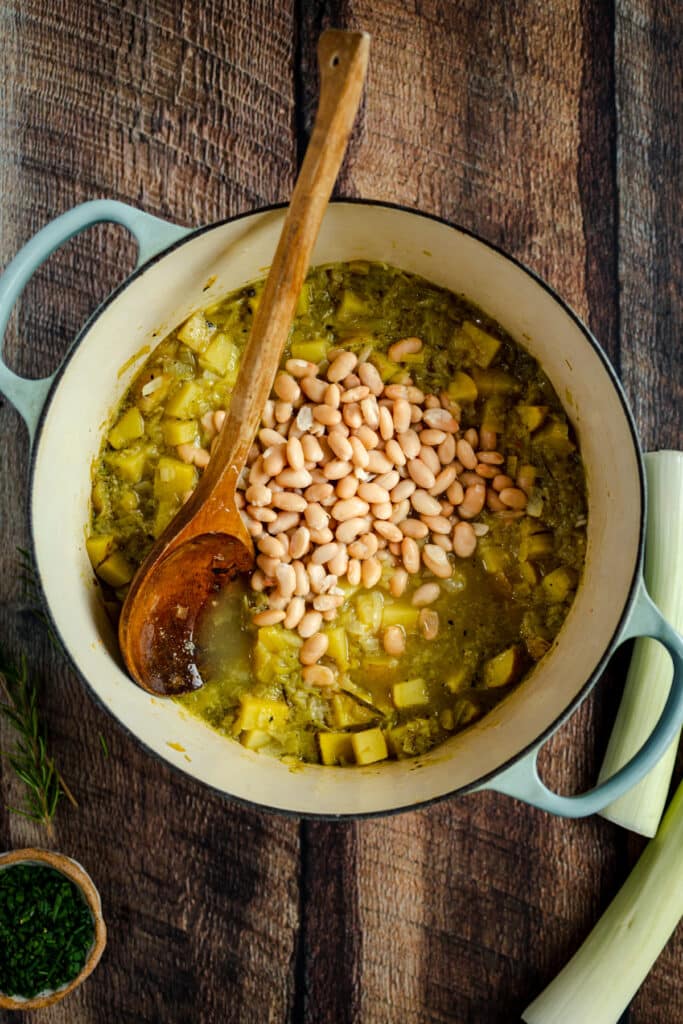 A pot of beans and leeks on a wooden table.