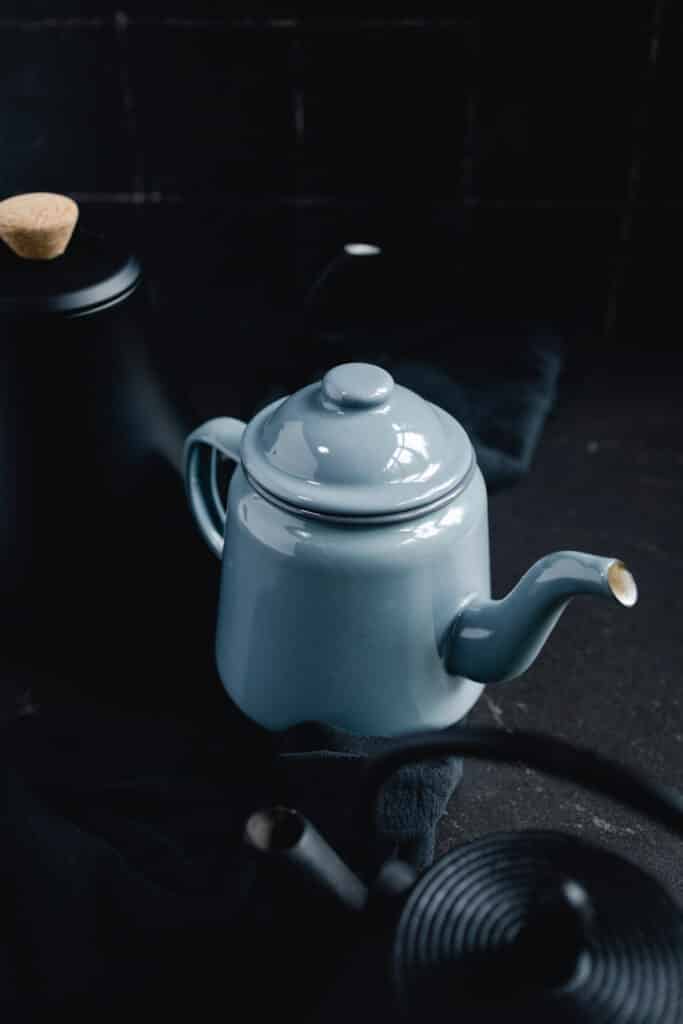 A blue teapot and a black teapot on a table.