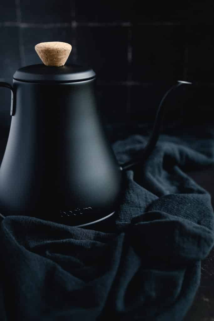 A black tea kettle sitting on a black cloth.