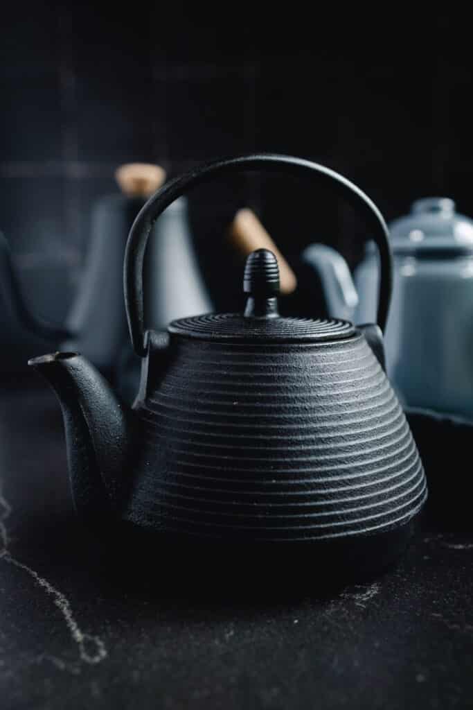 A black teapot sits on a black countertop.