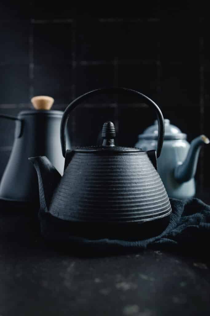 Two black teapots on a black background.