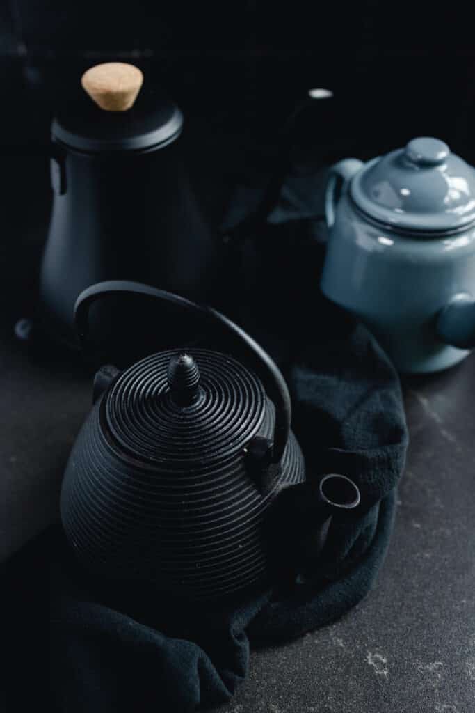A black teapot and a blue teapot on a black cloth.