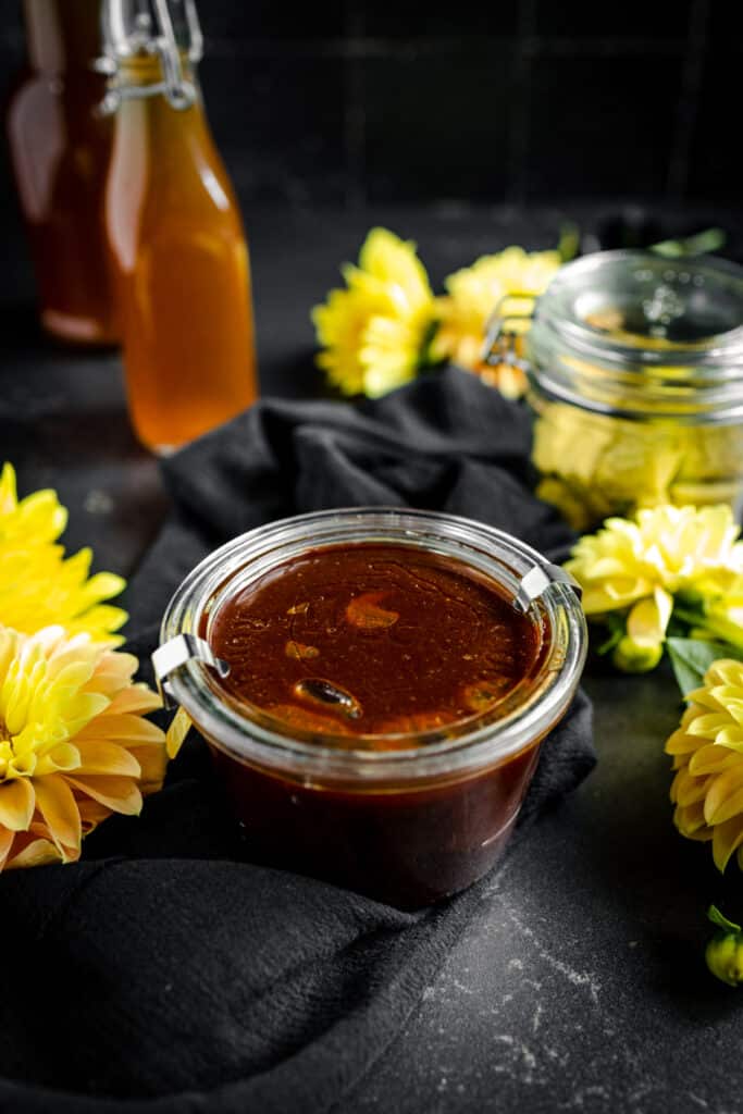 A jar of honey on a table next to yellow flowers.