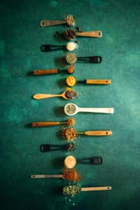 A group of teaspoons with different spices on a green background.