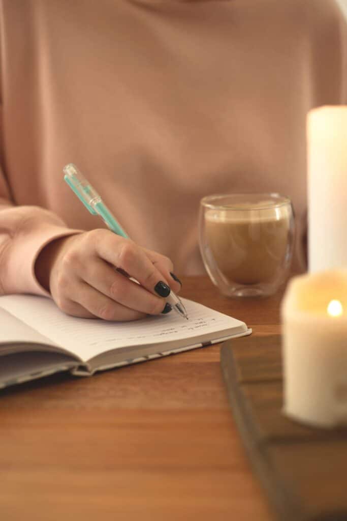 A woman writing in a notebook next to a candle.