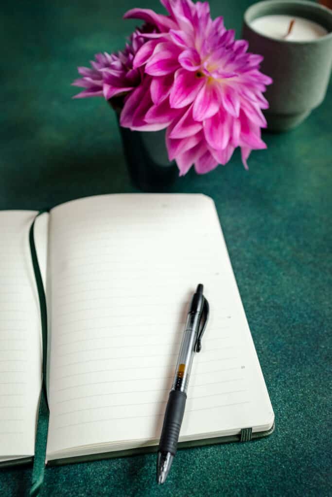 A notebook with a pen and flowers on a green table.
