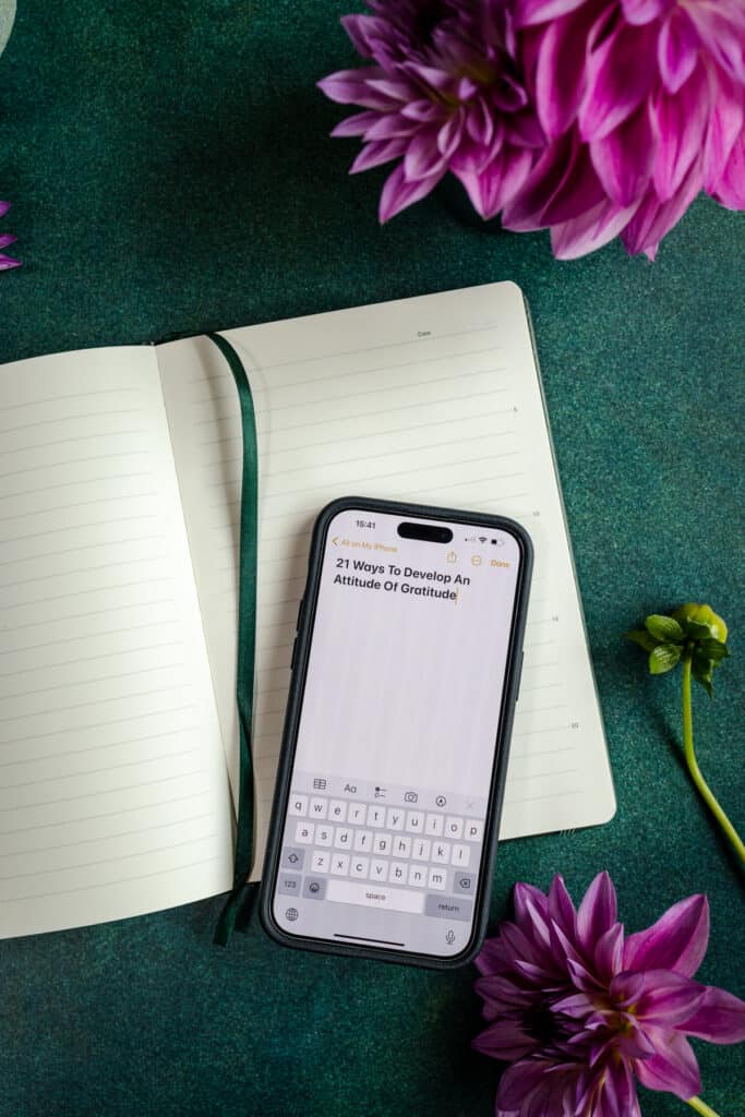 A phone with a notepad and flowers on a table.