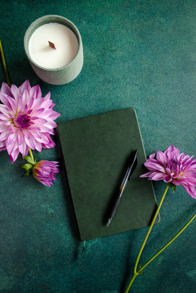 A green notebook with purple flowers and a candle on a green table.