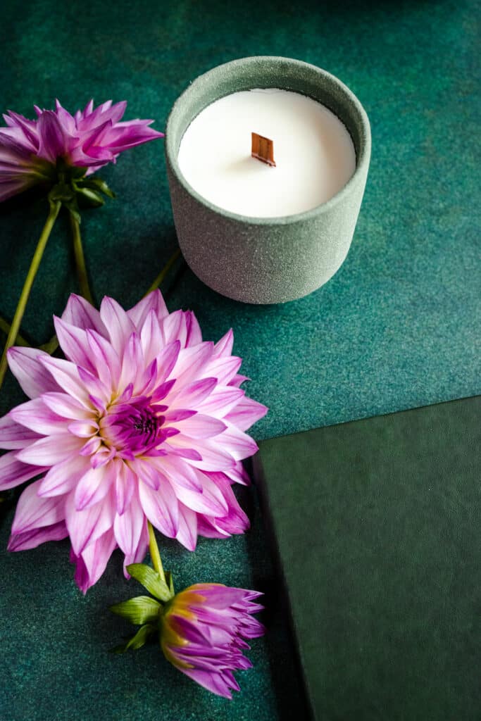 A candle, a book and flowers on a green table.