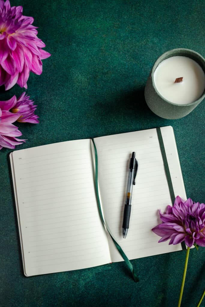 An open notebook with purple flowers and a candle on a green table.