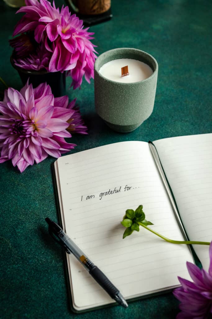 A notebook with a candle and flowers on a green table.