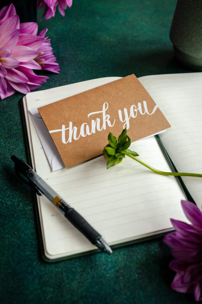 A thank you note with flowers and a pen on a notebook.