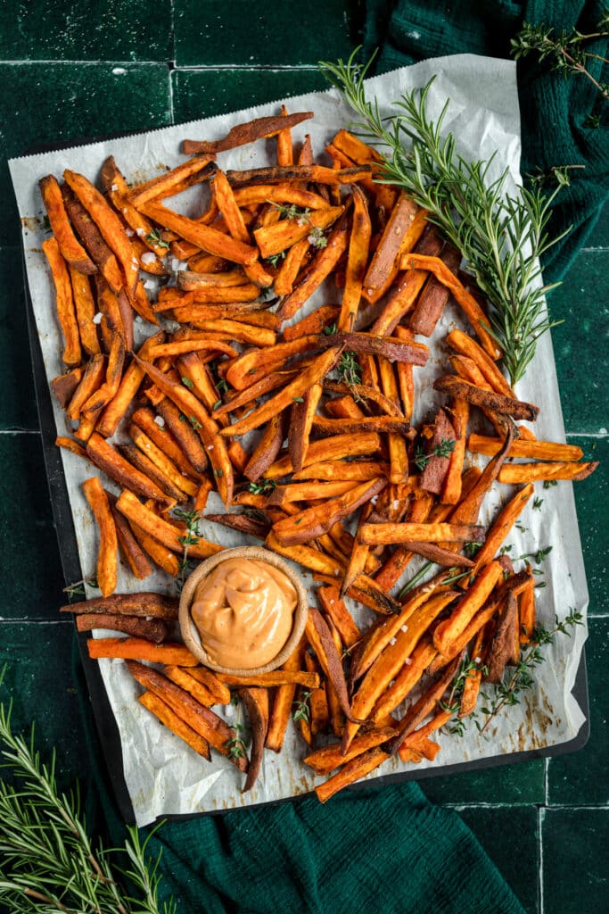 Sweet potato fries on a baking sheet with rosemary sprigs.