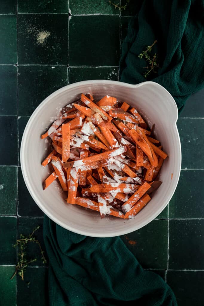 Sweet potato fries in a white bowl on a green tile.