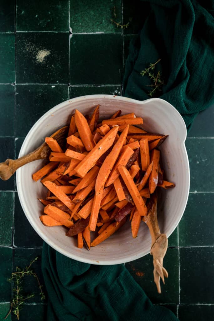 Sweet potato fries in a white bowl on a green tiled floor.