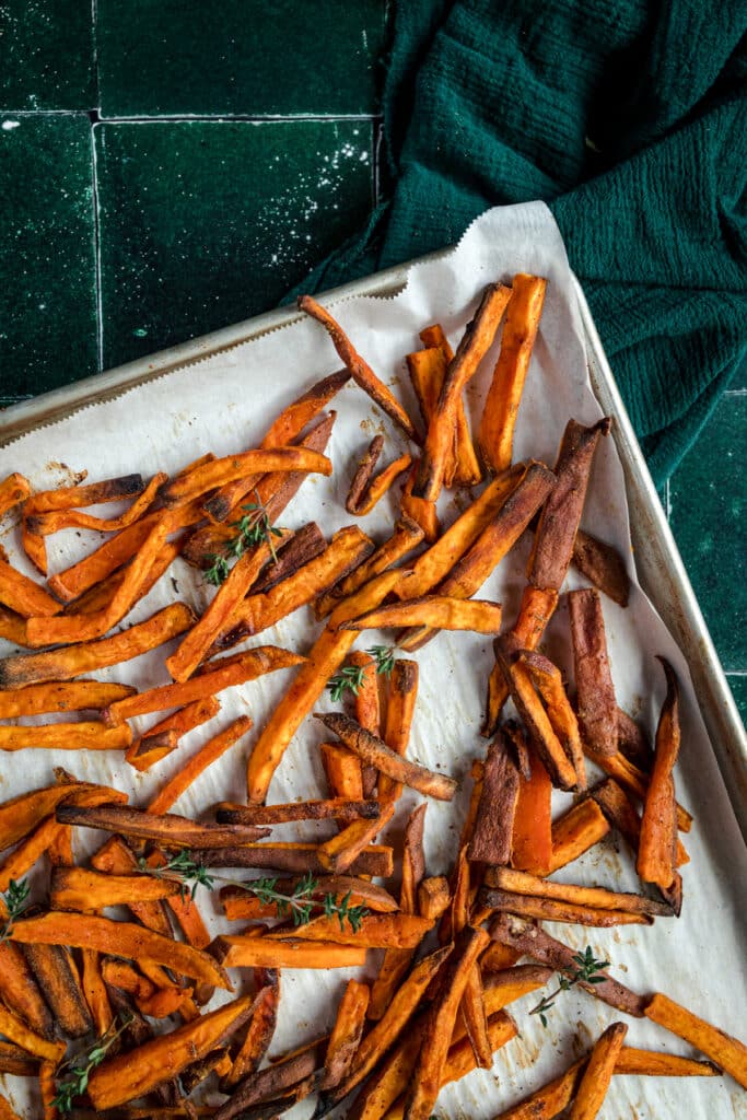 Sweet potato fries on a baking sheet with sprigs of thyme.