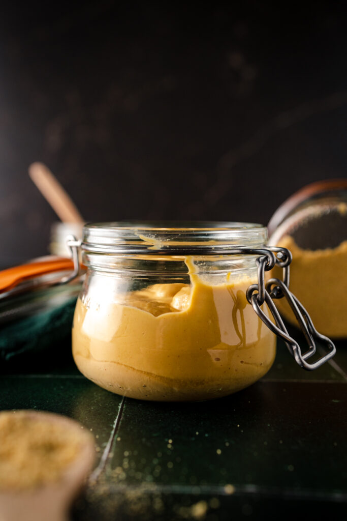 A jar of mustard on a table next to a wooden spoon.